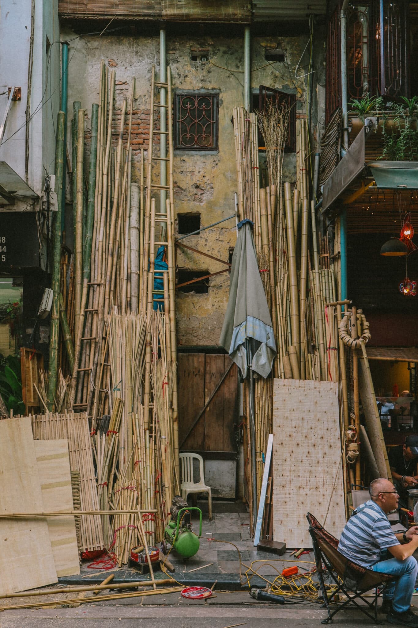 Hanoi alleyway with bamboo, ladder, and man sitting. Discover Hanoi hidden gems off the beaten track.