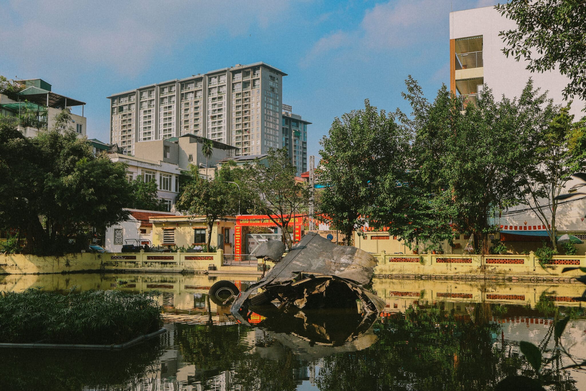 Hanoi hidden gem: US bomber wreckage in Huu Tiep Lake, Vietnam, with buildings in background.