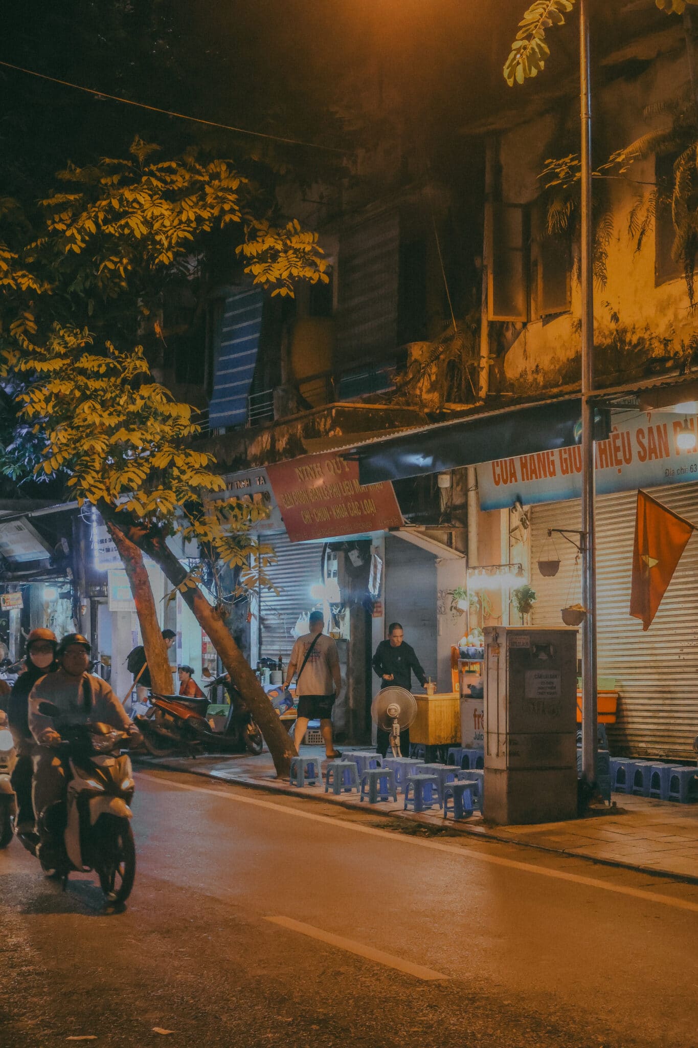 Hanoi street scene at night with scooters and food vendors. Discover what to do in Hanoi, Vietnam.