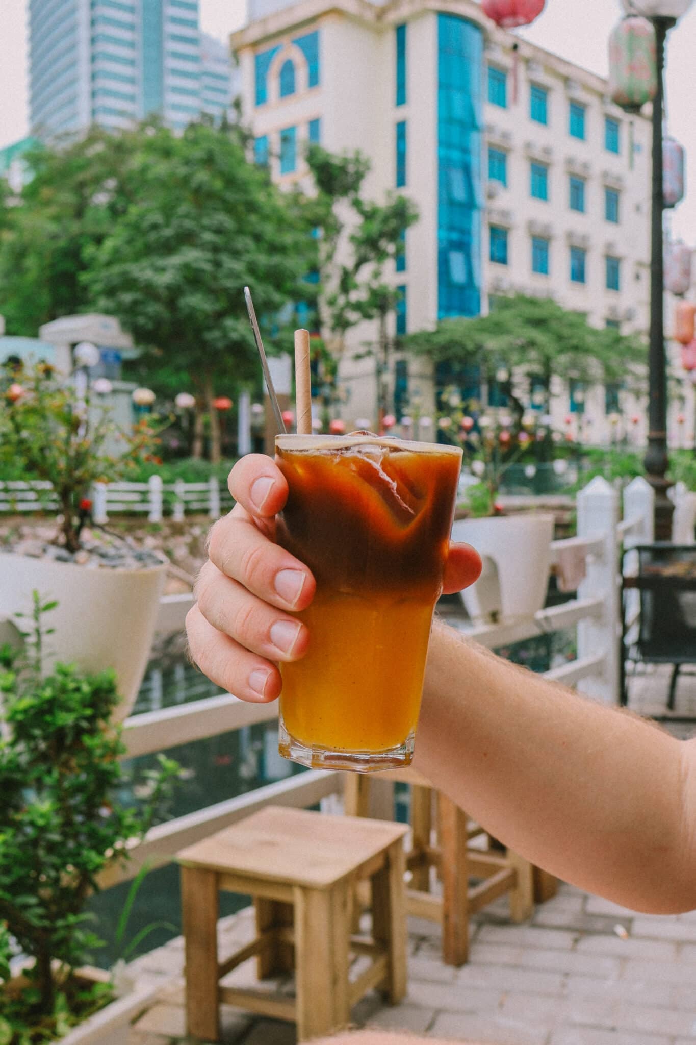 Hand holding iced coffee with orange juice in Hanoi, Vietnam. What to do in Hanoi for unique experiences.