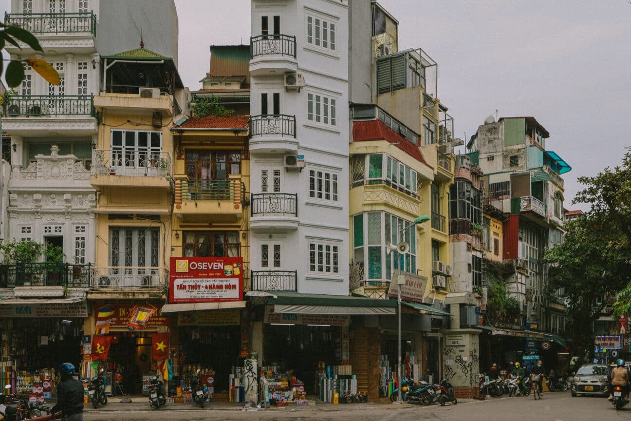 Hanoi street scene with colorful buildings and motorbikes. OSEVEN sign visible.