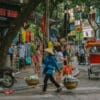Hanoi street scene with vendor carrying baskets. "Made in Viet Nam Outlet Factory" sign visible. Things to do in Hanoi.