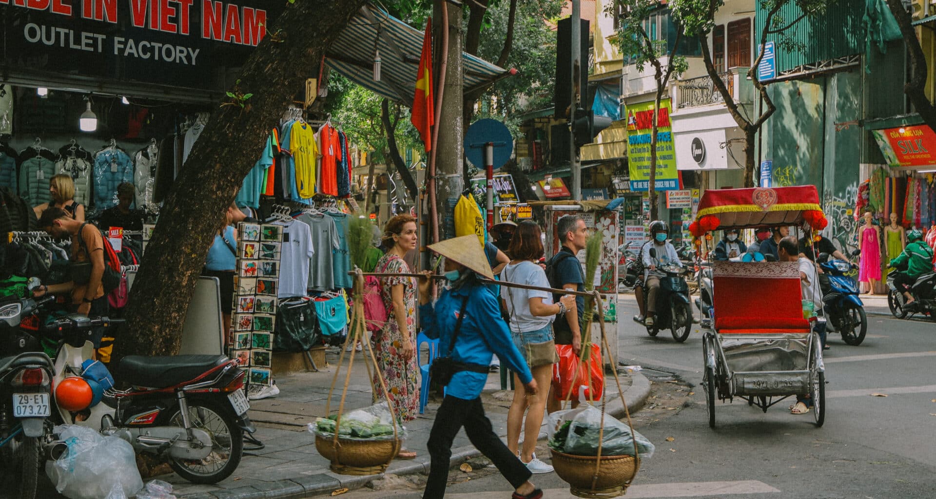 Hanoi street scene with vendor carrying baskets. "Made in Viet Nam Outlet Factory" sign visible. Things to do in Hanoi.