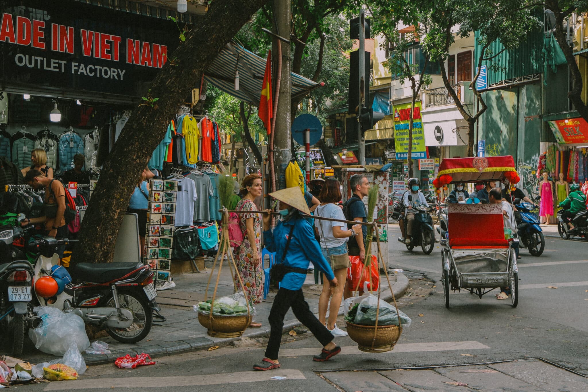 Hanoi street scene with vendor carrying baskets. "Made in Viet Nam Outlet Factory" sign visible. Things to do in Hanoi.