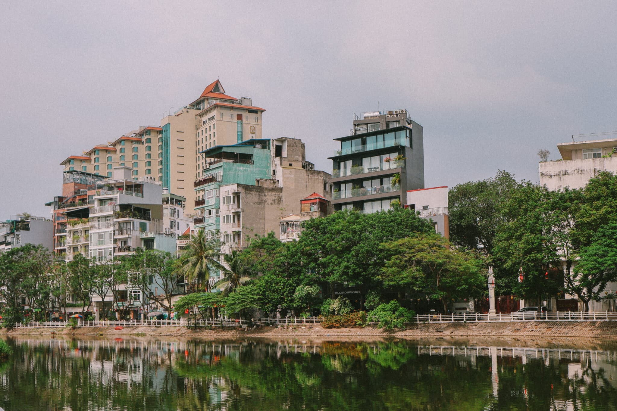 Hanoi skyline reflected in Truc Bach Lake, Vietnam, with trees and buildings.