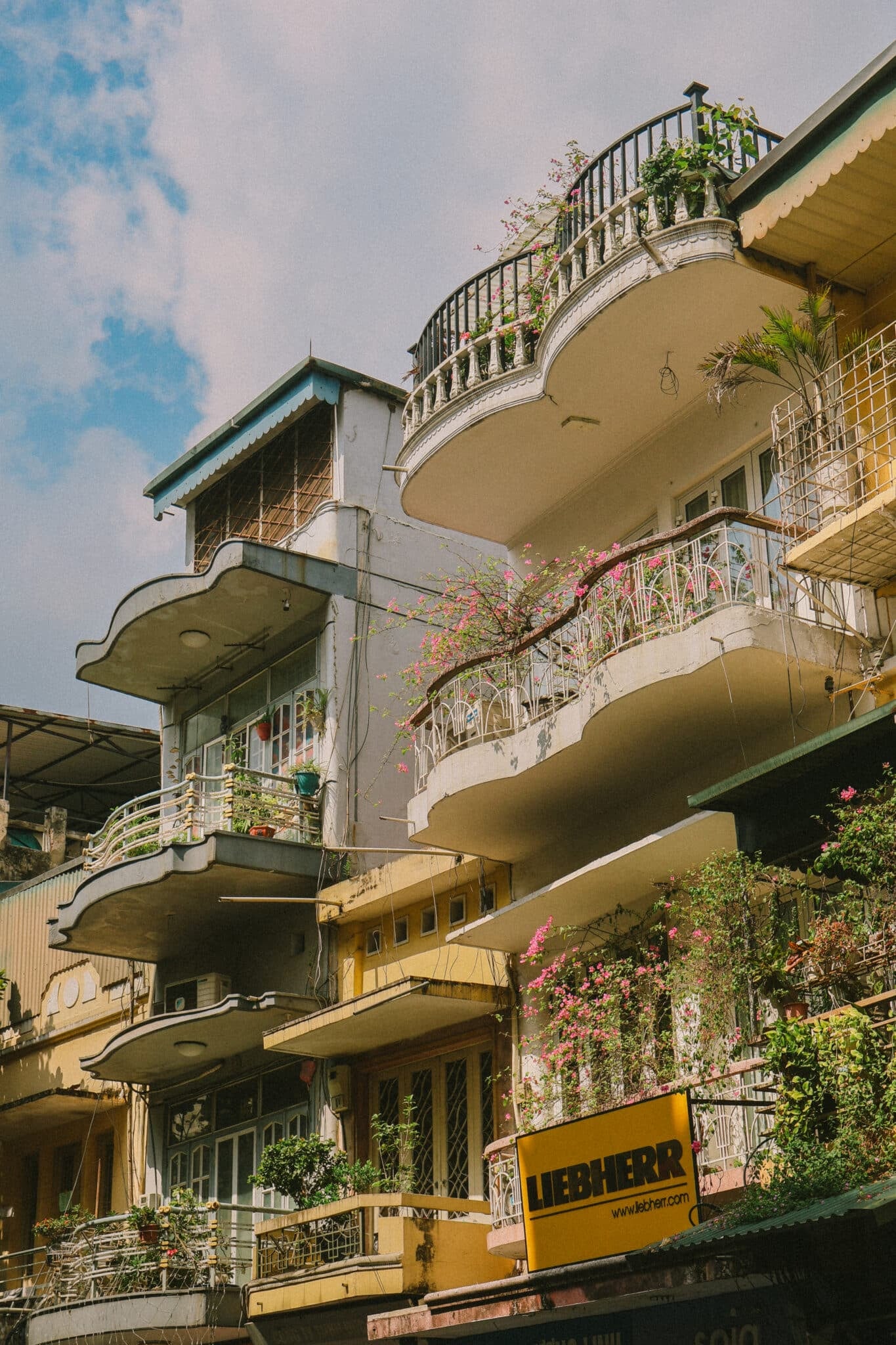 Balconies with plants on an old building in Hanoi, Vietnam. Liebherr sign visible.