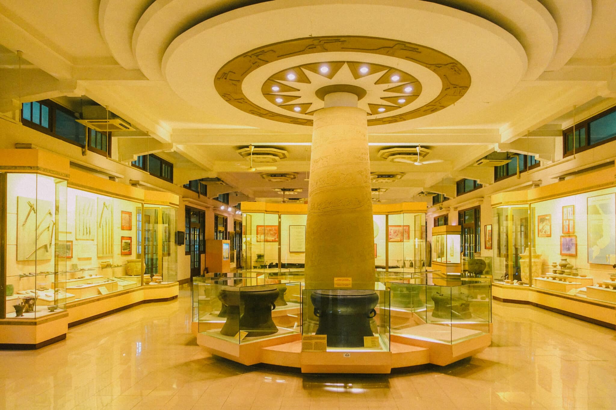 Interior of a Hanoi museum, showcasing artifacts in glass displays around a central pillar. #HanoiMuseums