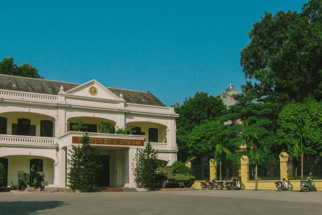 Vietnam Military History Museum in Hanoi with tank and motorcycles. "Bảo tàng Lịch sử Quân sự Việt Nam" text.