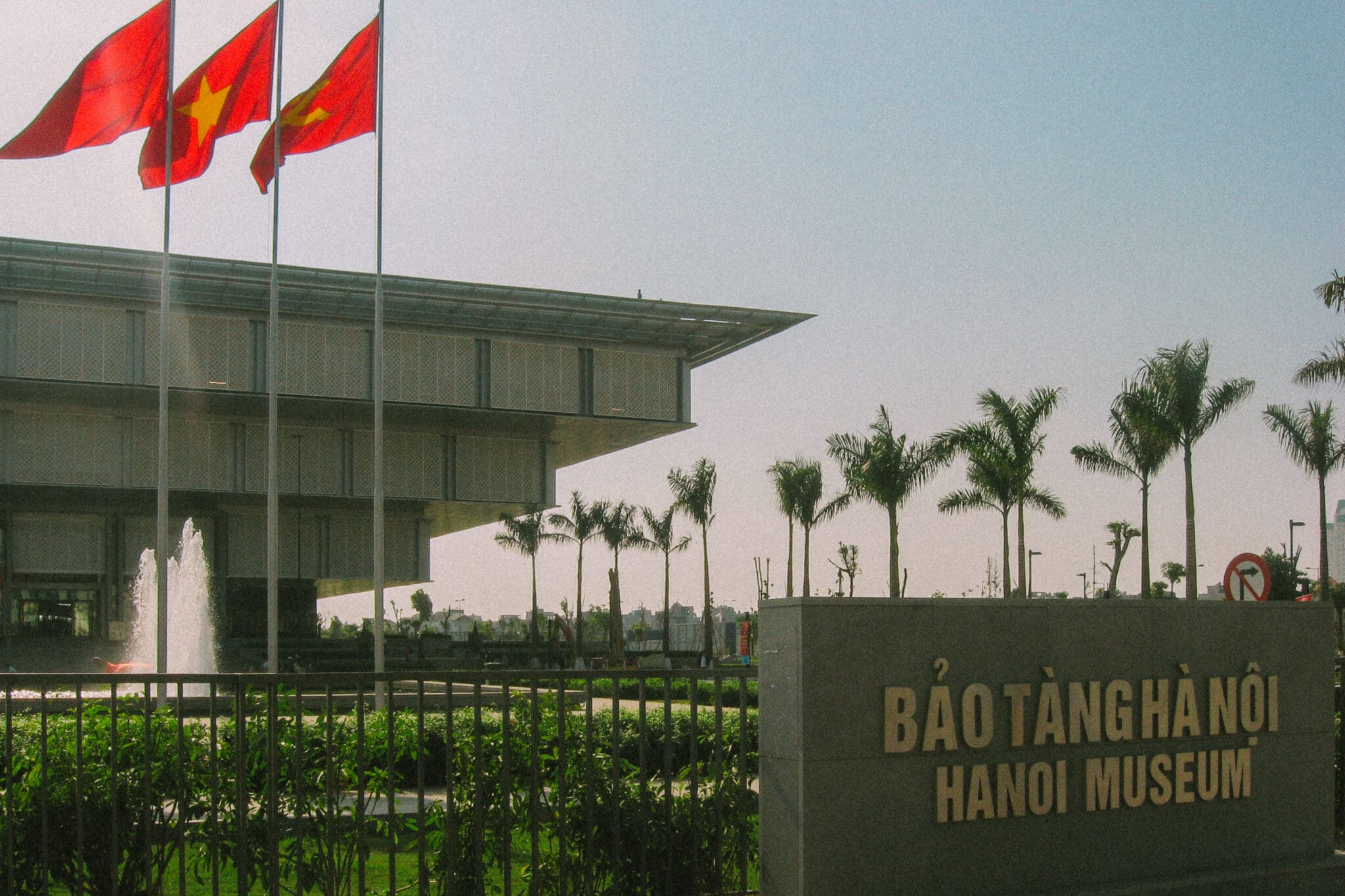 Hanoi Museum exterior with Vietnamese flags and sign. "Bảo Tàng Hà Nội - Hanoi Museum