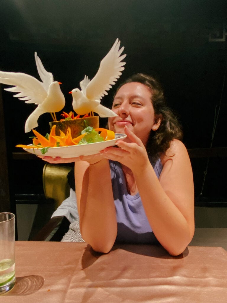Woman smiles at a fruit platter with dove decorations on a private Ha Long Bay cruise.