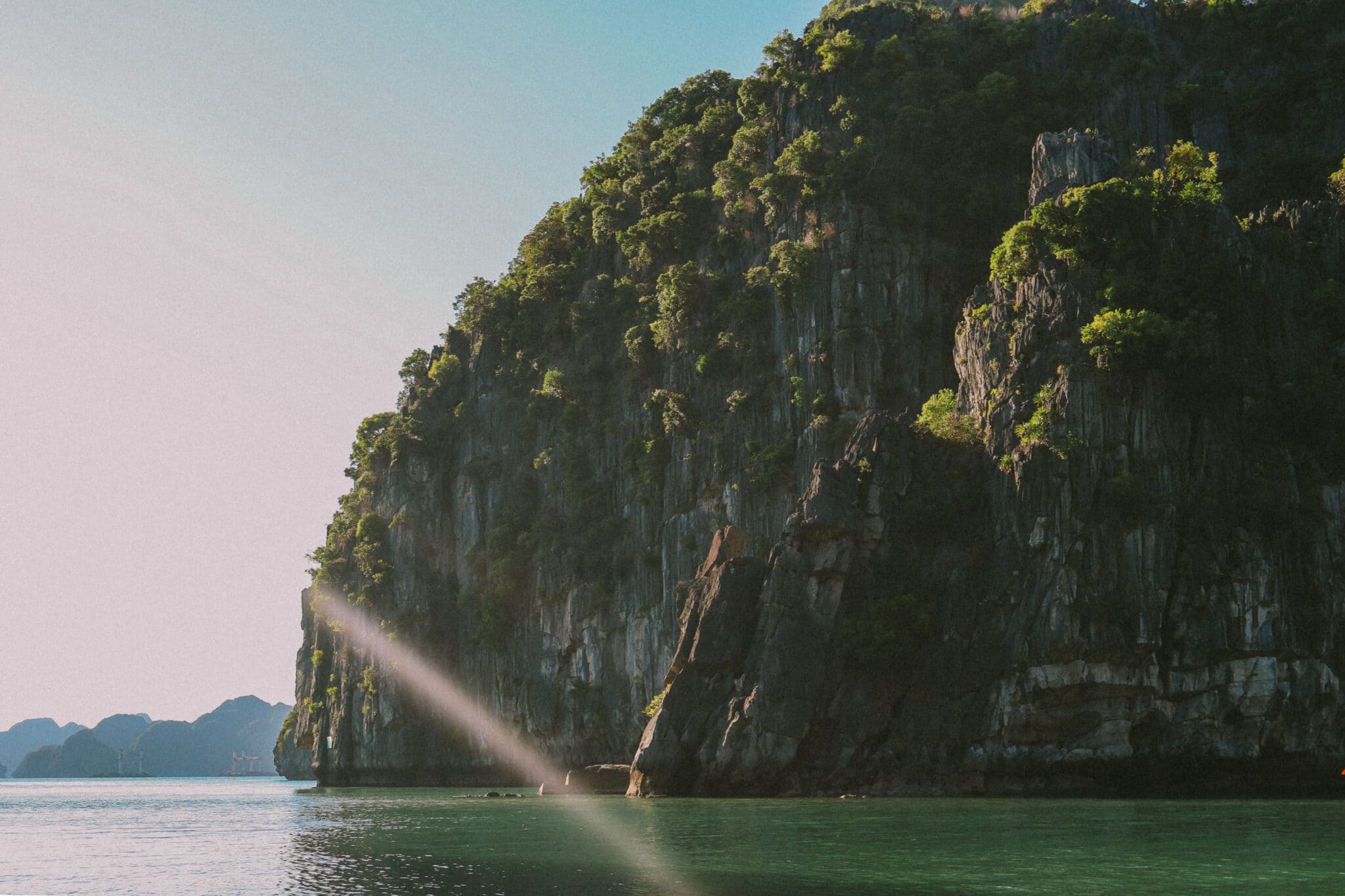 Sunbeam hitting a lush green karst cliff on a private Ha Long Bay cruise, L'Amour Junk.
