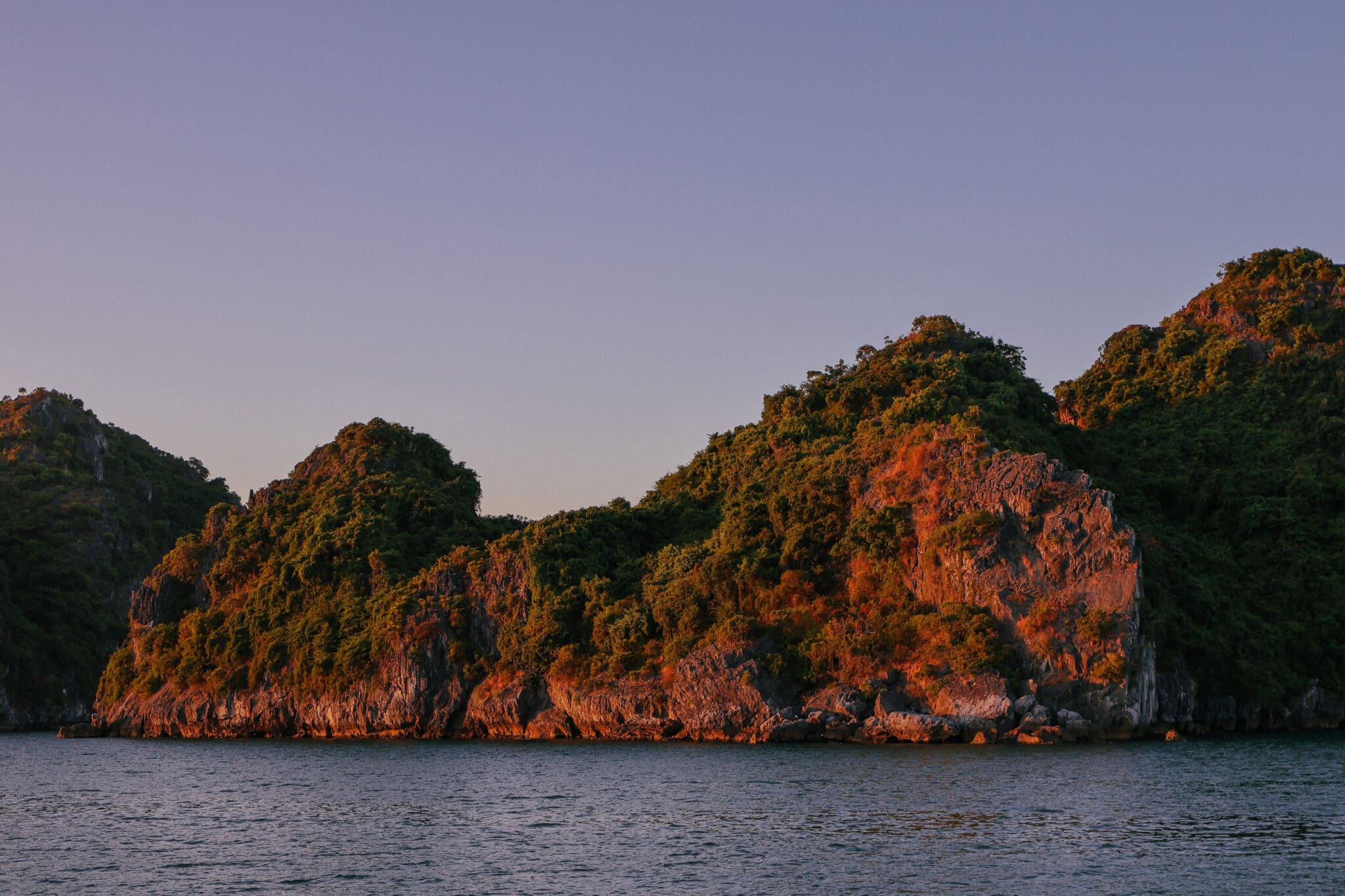 Lush green islands in Ha Long Bay at sunset, seen from a private cruise.