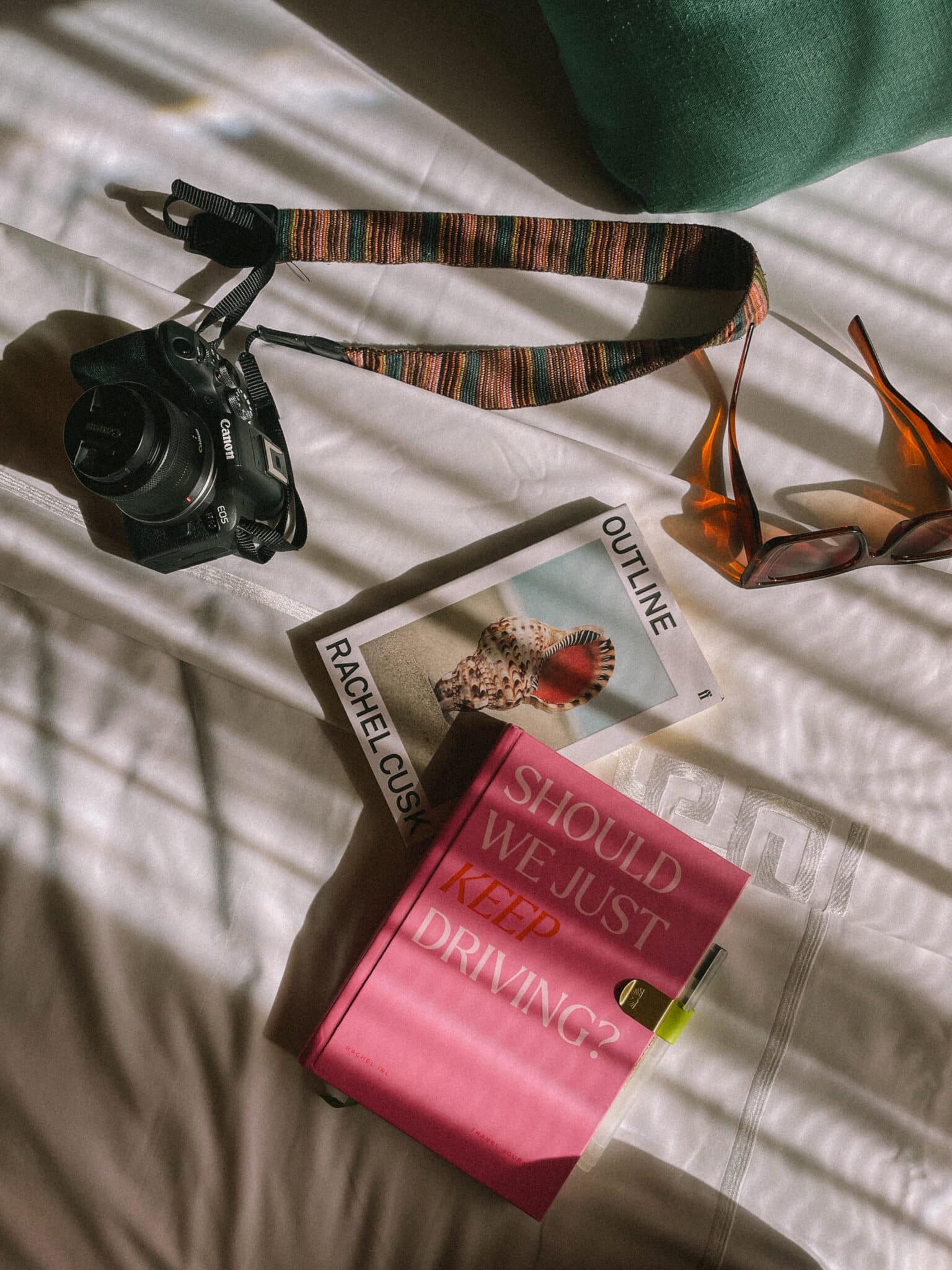 Canon camera, books, and sunglasses on a white sheet, hinting at travel.