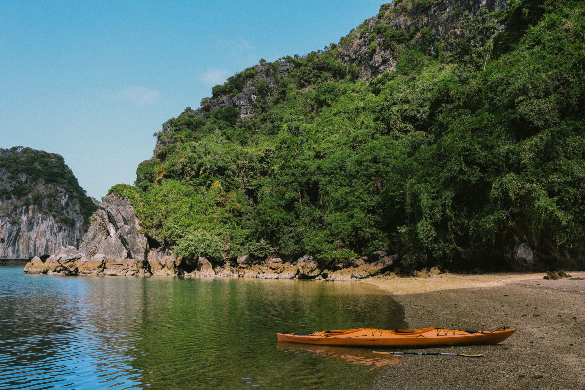 Orange kayak on a sandy beach in Ha Long Bay, with lush green cliffs.