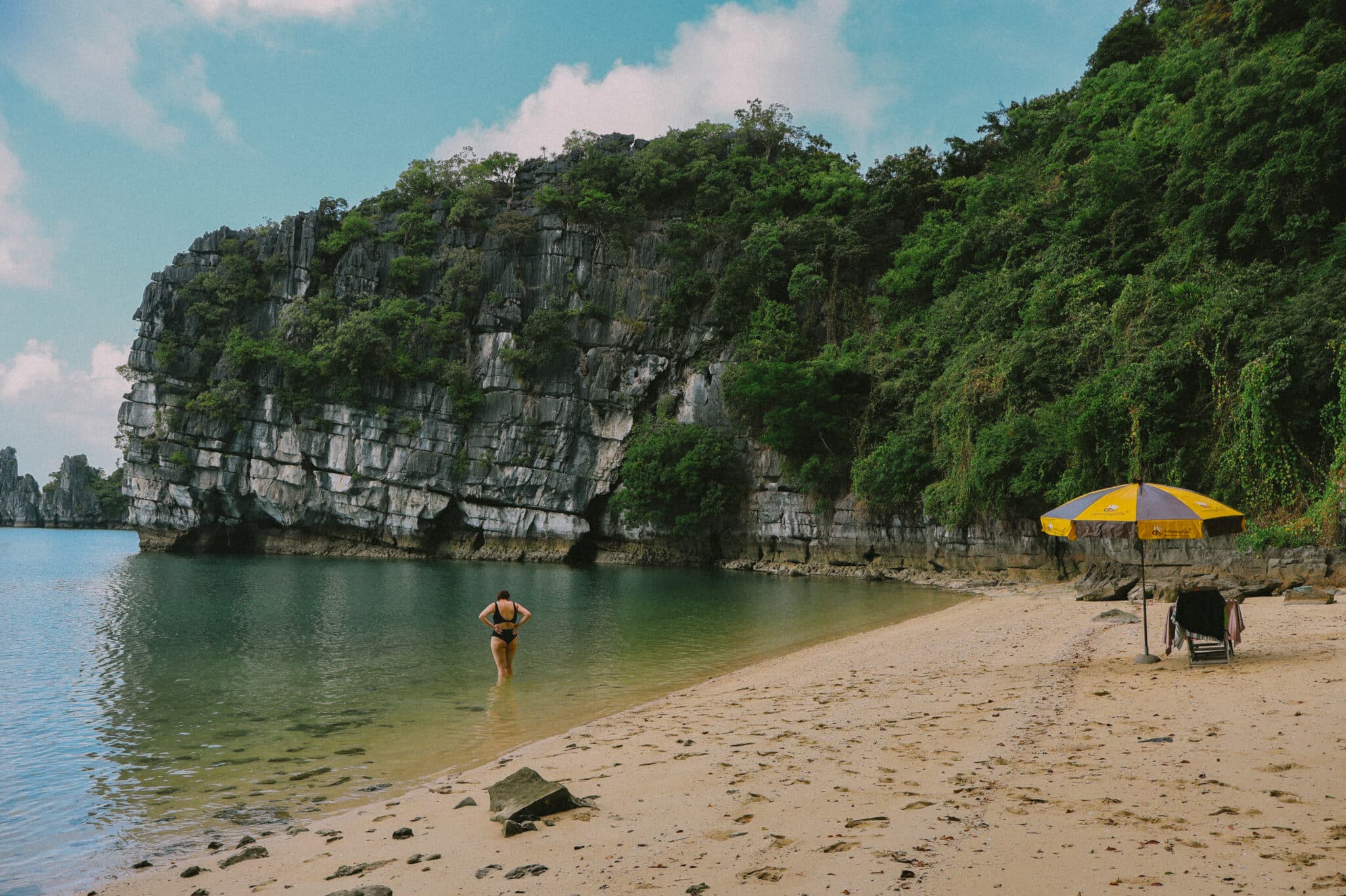 Woman wading into calm water on a secluded beach during a private Ha Long Bay cruise on L'Amour Junk.