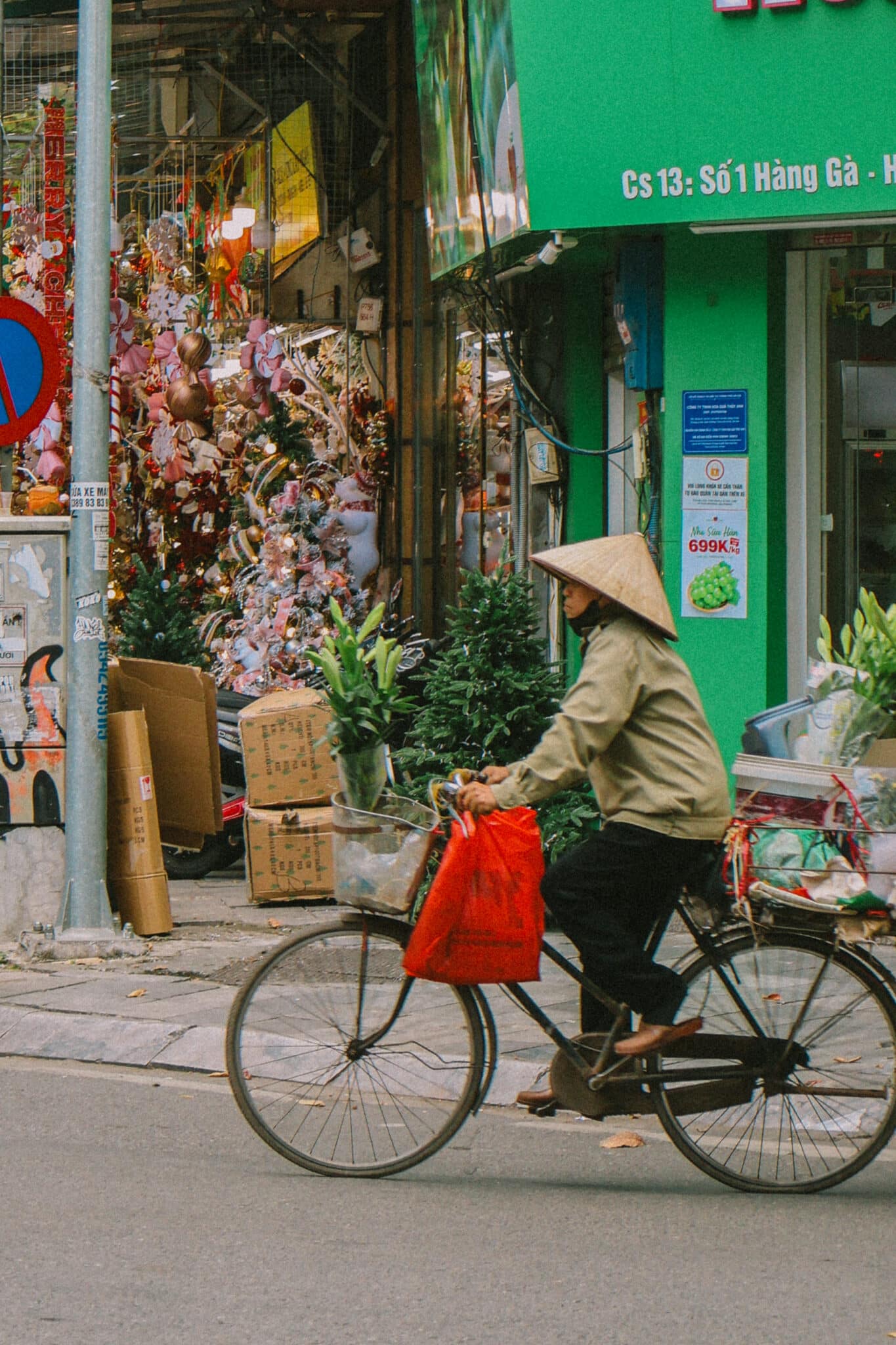 Person in conical hat cycles through Hanoi Old Quarter, past decorated shops.