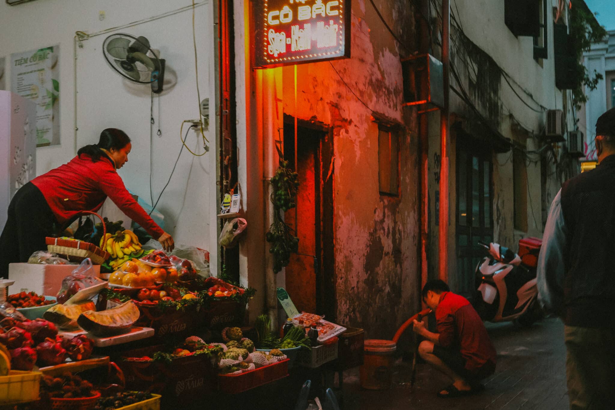 Hanoi Old Quarter street scene at night with fruit stall and locals.