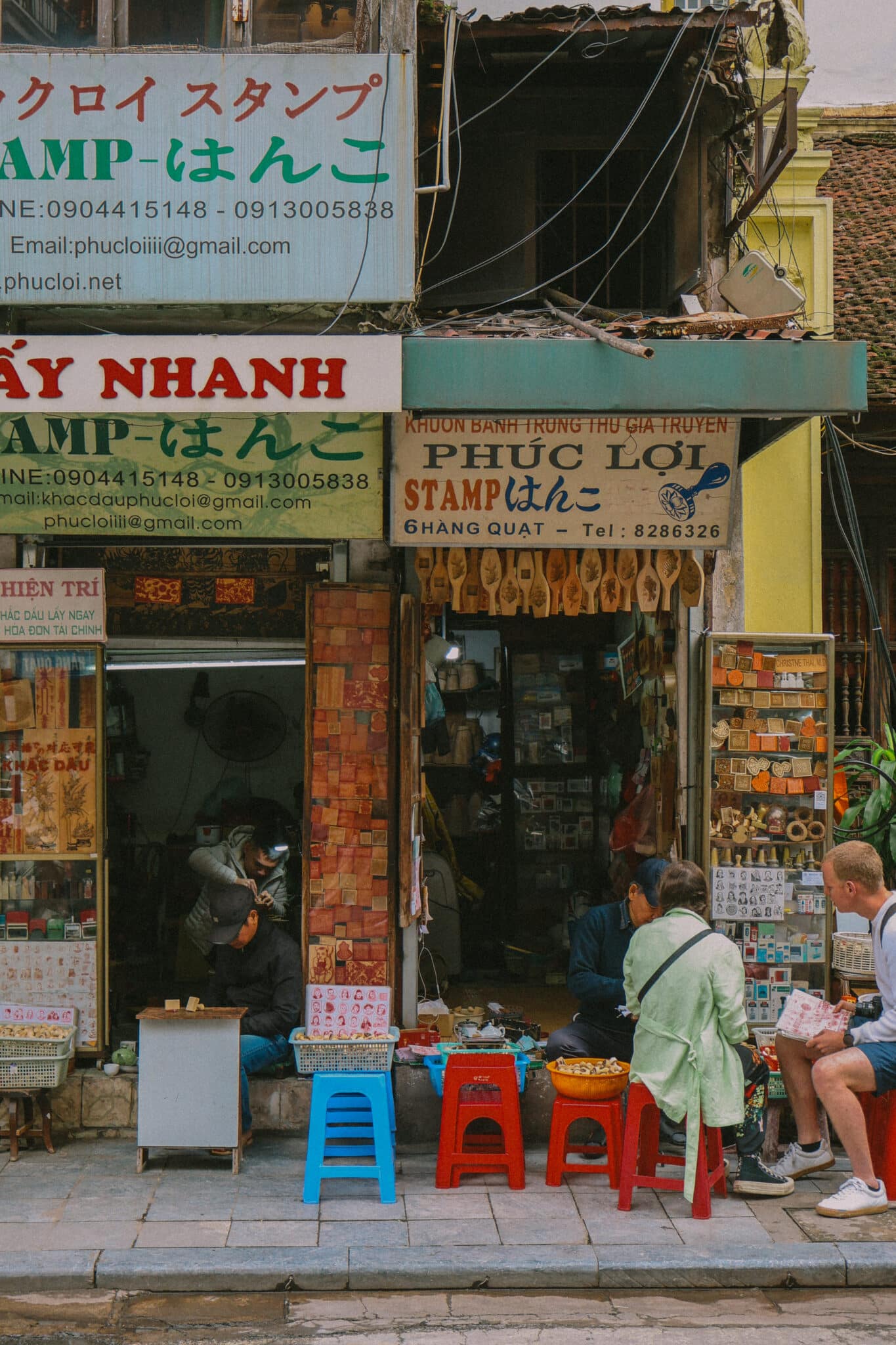 Hanoi Old Quarter shops with signs in Vietnamese and Japanese, people browsing.