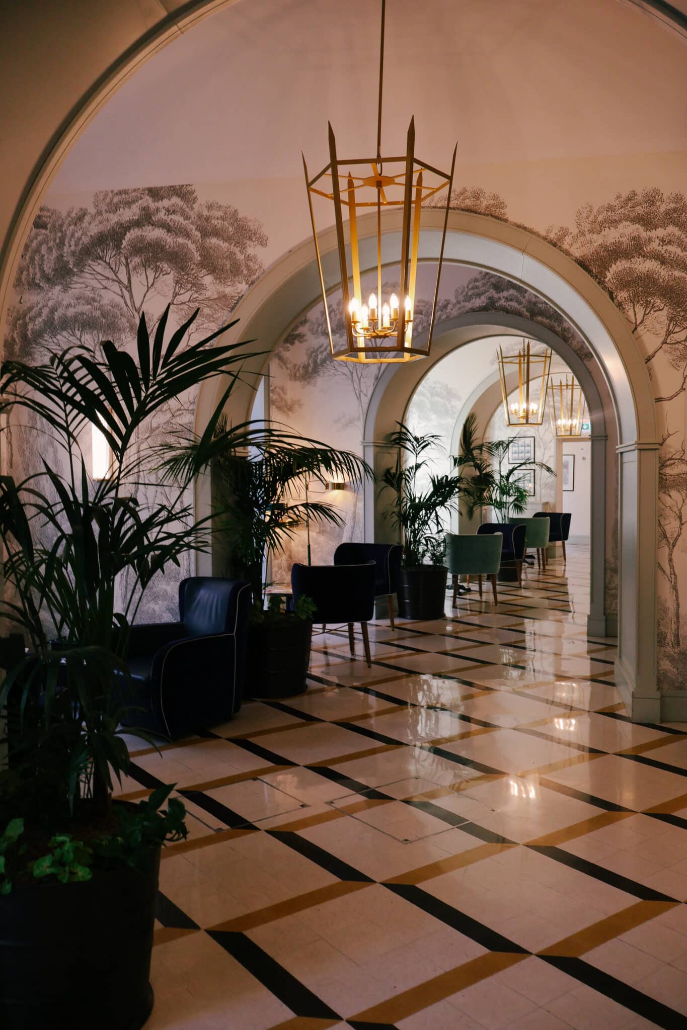 Lobby of hotel in Rome with tiled floor, black and white checkered pattern, potted plants, chairs, and chandeliers