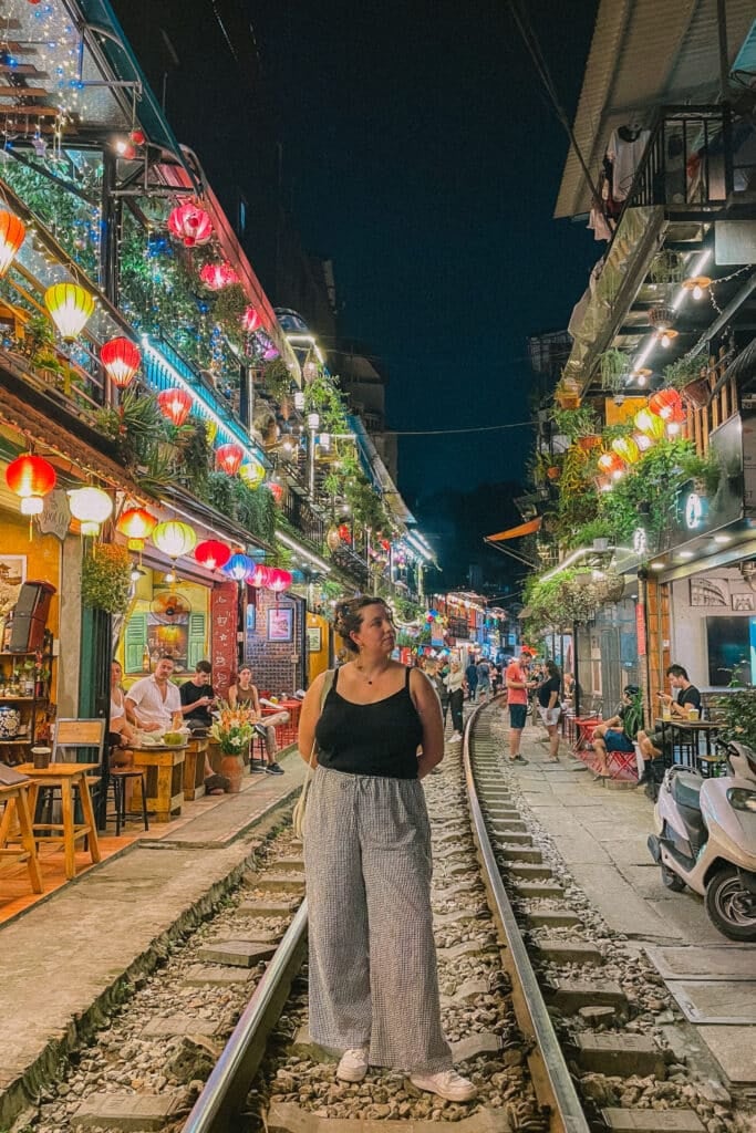 Woman on train tracks in Hanoi Old Quarter at night, lit by lanterns