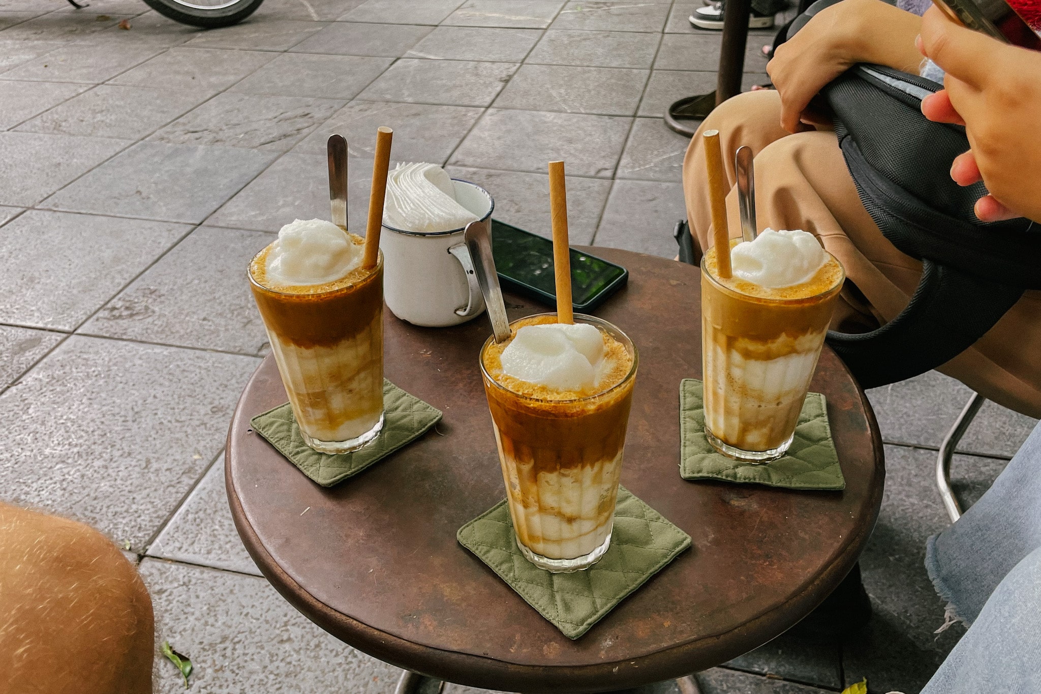 Three iced coconut coffee drinks with foam and straws on a table at a Hanoi cafe, Cong Ca Phe