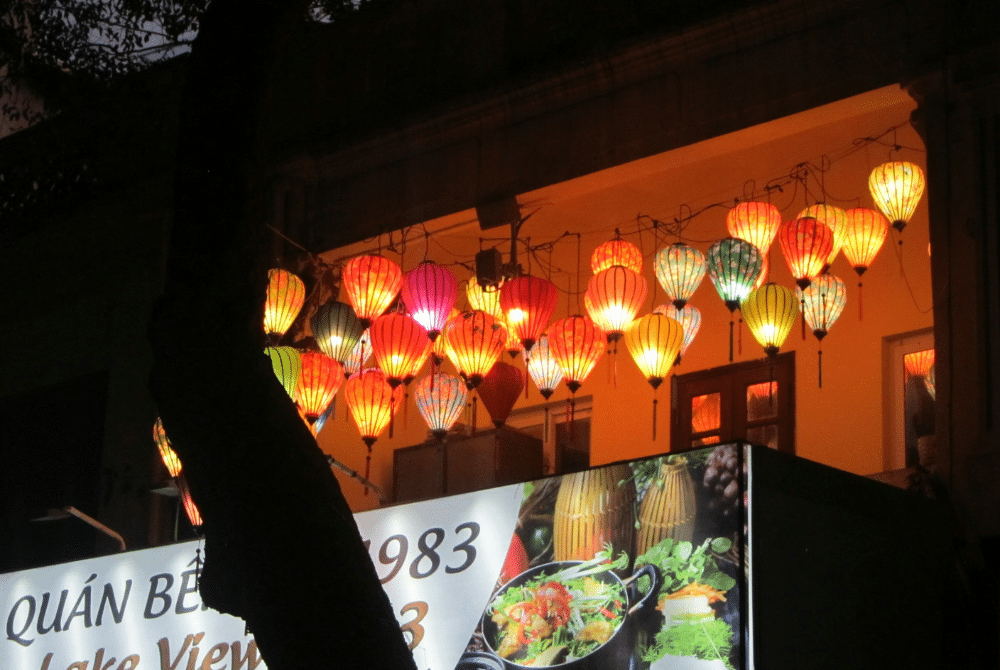 Colorful lanterns illuminate a Hanoi restaurant facade, suggesting a vibrant dining experience.