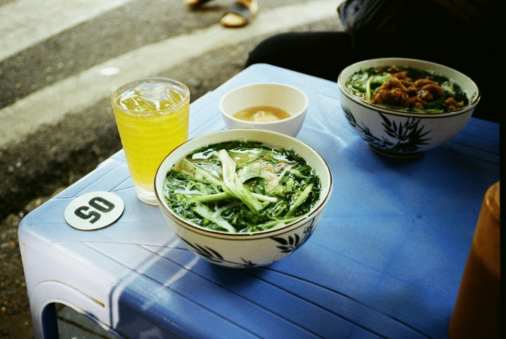 Hanoi street food: bowls of pho and a yellow drink on a blue table at Pho Gia Truyen